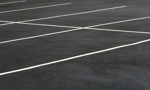 Empty parking lot with clean, black asphalt featuring precise white lines marking parking spaces. The scene is orderly and minimalistic.