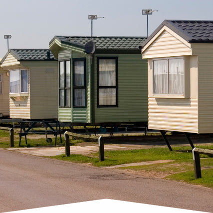 WindowsRow of colorful mobile homes on a sunny day, lined up on a grassy area beside a paved road, conveying a serene, community-like atmosphere.